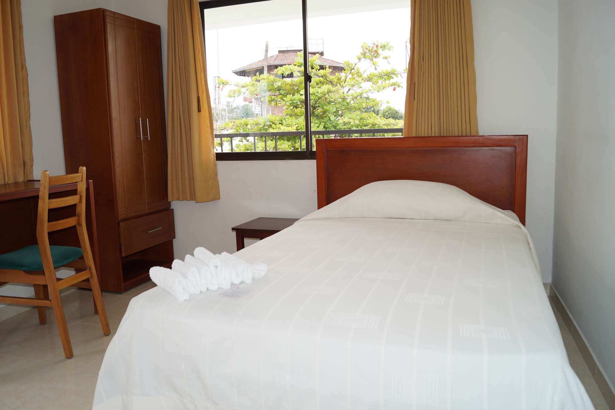 Habitación con cama individual, armario de madera y ventana hacia los jardines