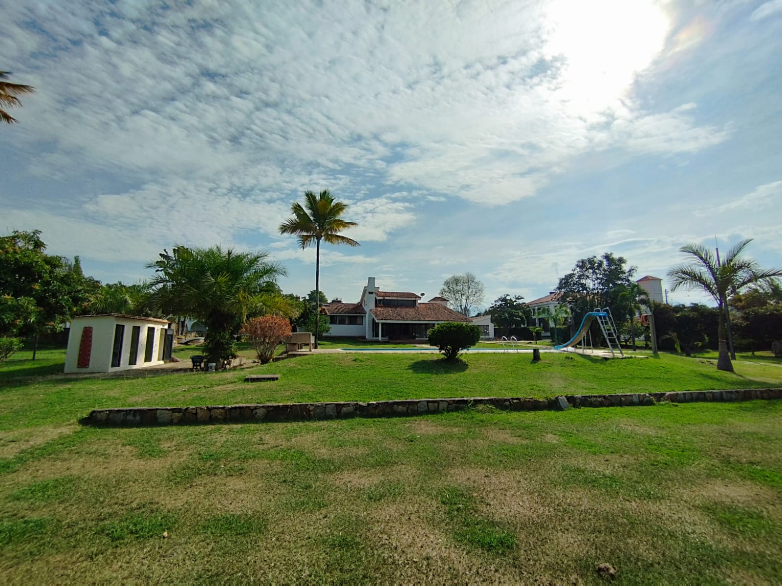 Amplia zona de césped con palmeras, jardines y edificios de la Casa Buenos Aires en Chinauta