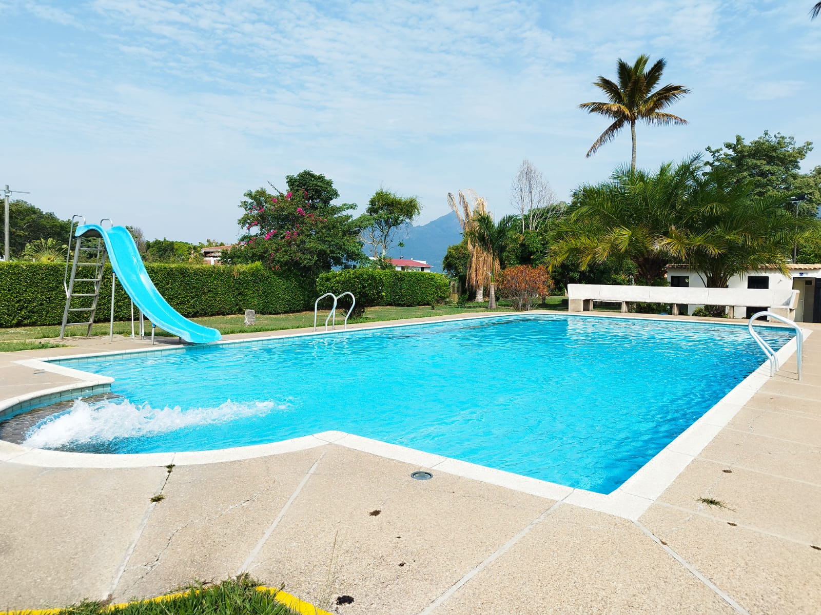 Piscina al aire libre con tobogán azul, rodeada de palmeras y jardines de la Casa Buenos Aires